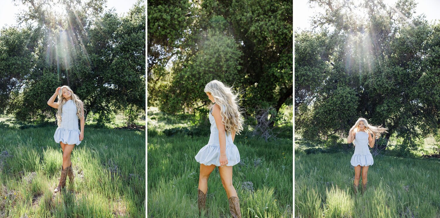 Blonde senior girl walking through vibrant green grass in denim dress and cowboy boots during Santa Clarita nature portraits.
