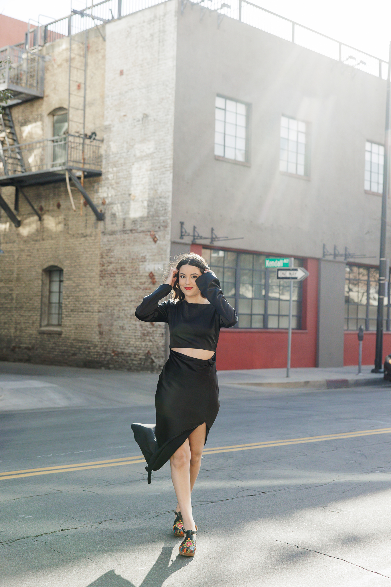 Senior girl in a black crop top and slit skirt walking down a Pasadena side street in golden light