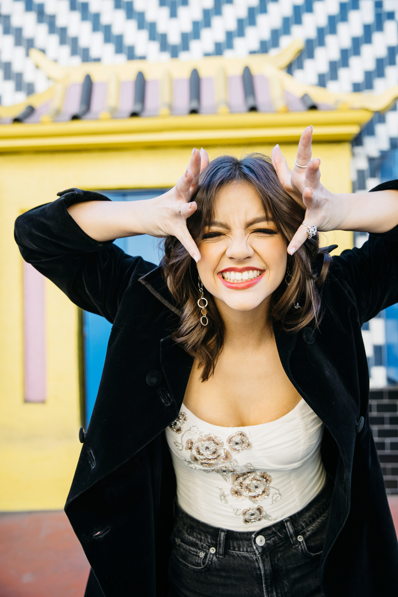 Senior girl grinning with her hands framing her face in front of a yellow pagoda in LA Chinatown