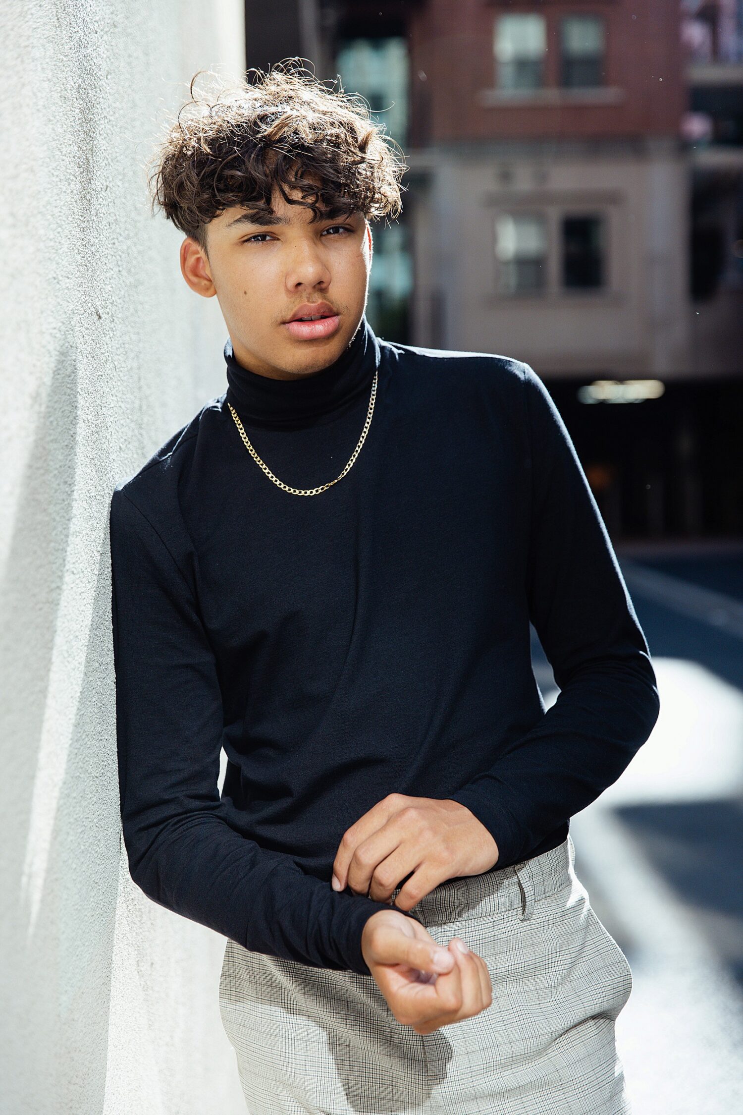 Senior guy in a black turtleneck and gold chain leaning against a wall in Downtown Los Angeles