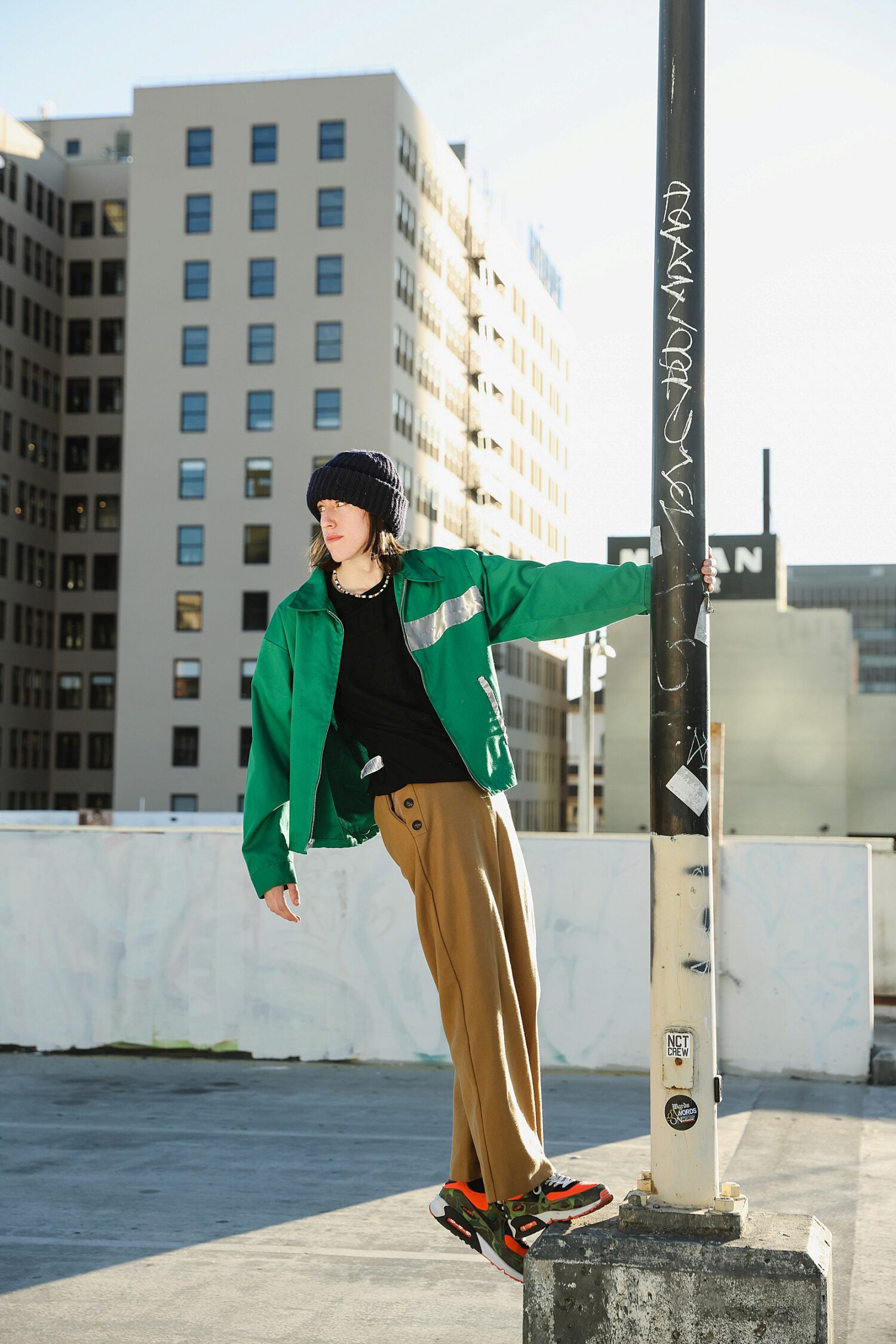 Senior guy leaning on a street pole on a Downtown LA rooftop with city buildings behind him