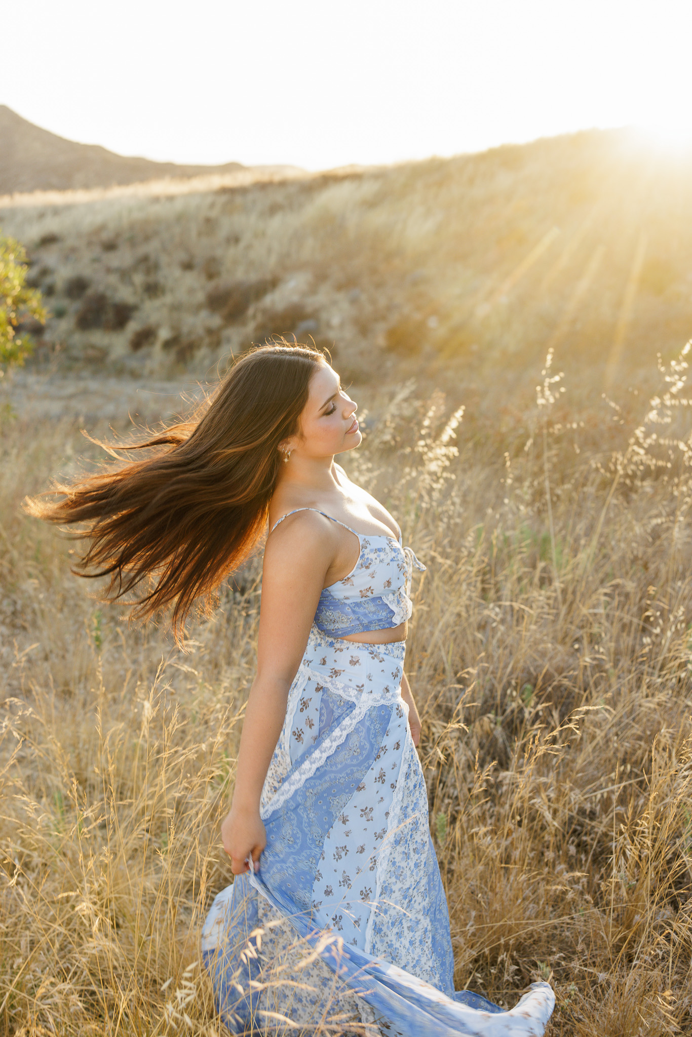 teen girl walking through wildflowers in her blue floral set and tan boots on a Santa Clarita hillside at golden hour