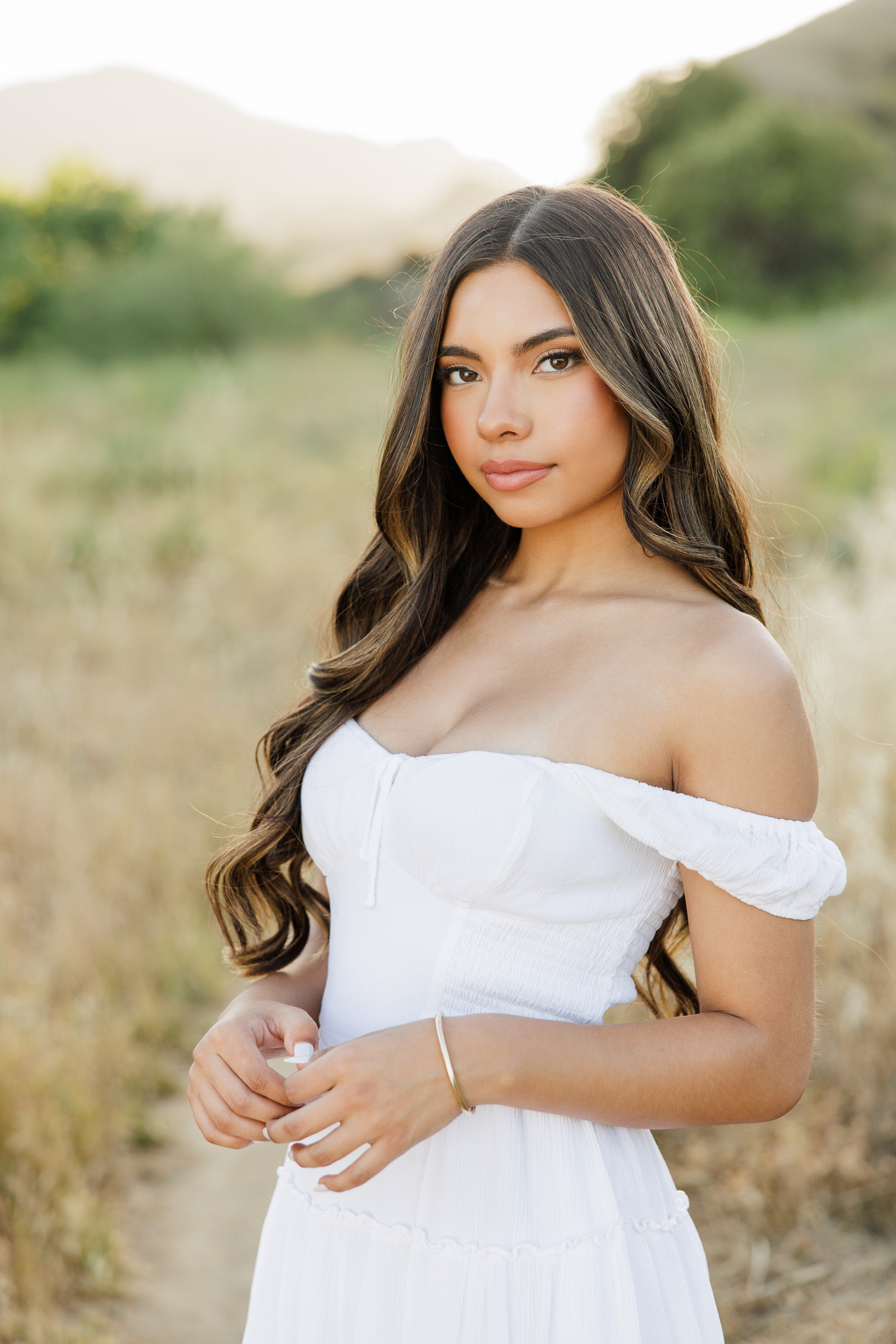 Senior girl in a white off-shoulder dress in a golden grass field with the Santa Clarita hills behind her