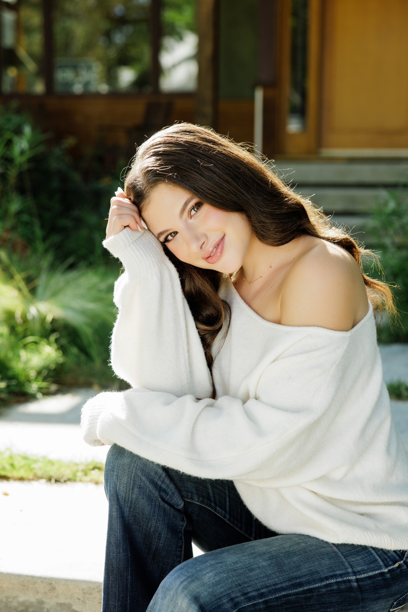 Buckley School senior in a white off-the-shoulder sweater standing in front of a warm wood and stone craftsman home with flowers in a Studio City neighborhood