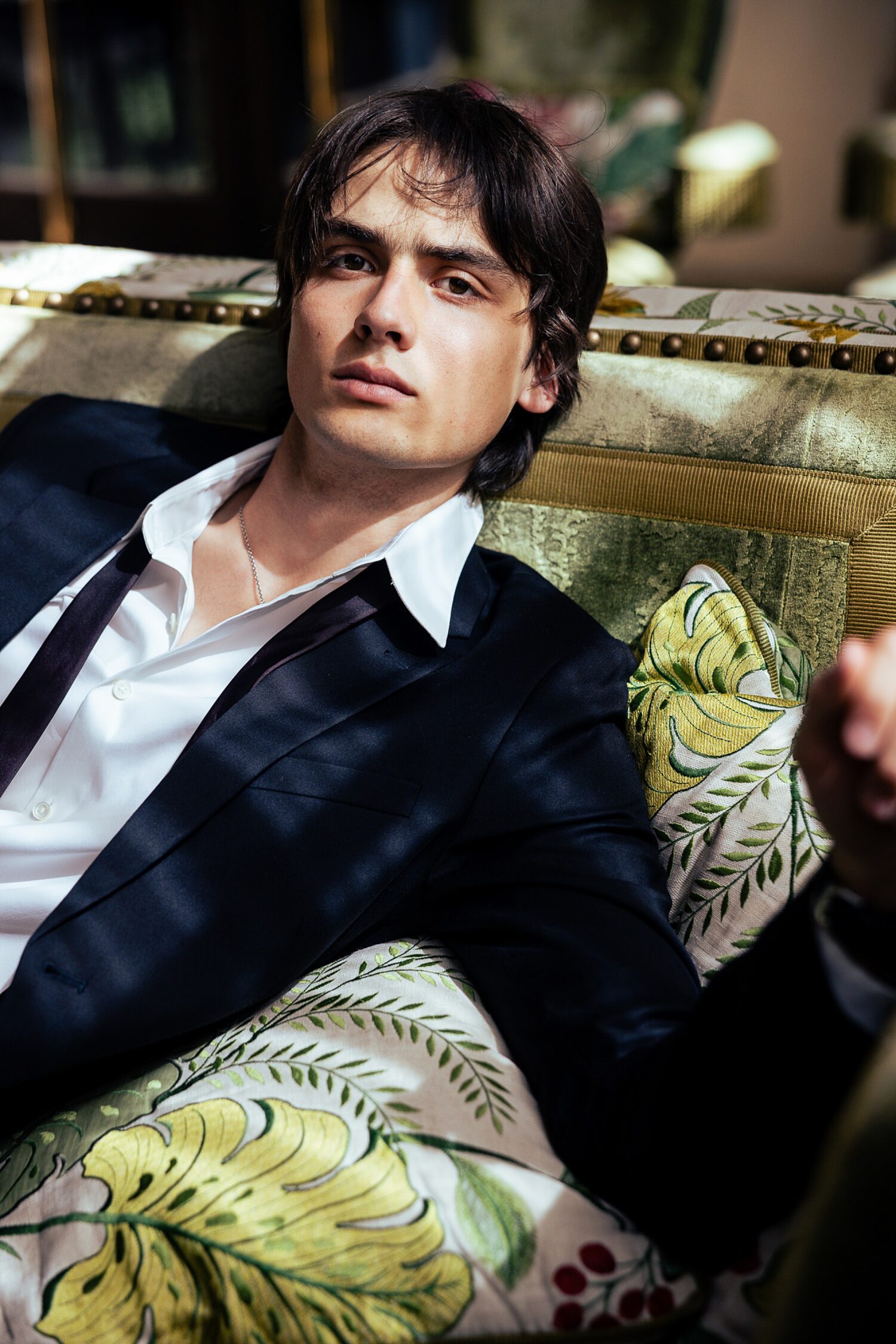 Guys senior pictures in Los Angeles of a senior guy in a navy suit and loosened tie leaning back on a floral couch