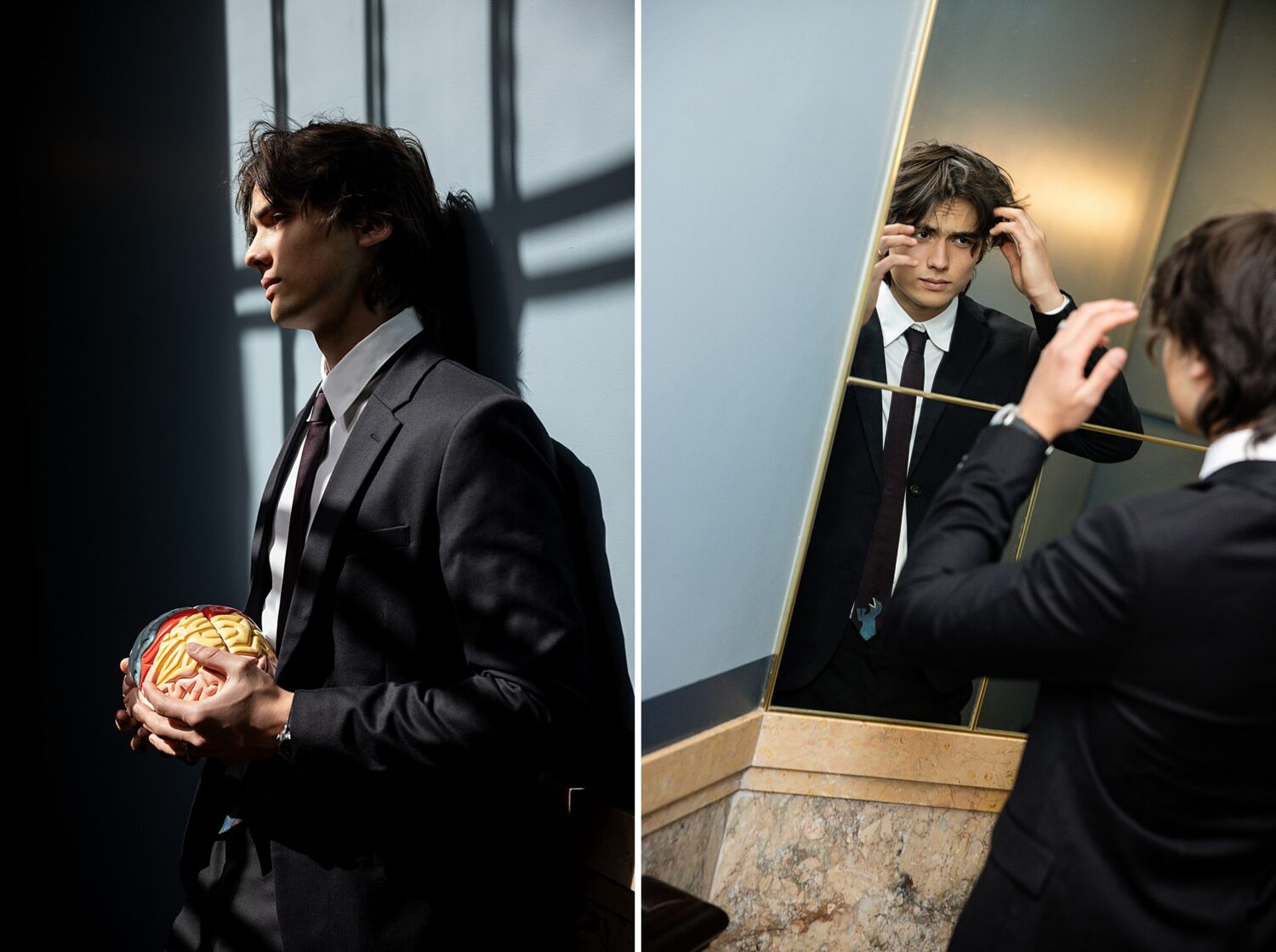 Guys senior pictures in Los Angeles of a senior guy in a black suit holding a brain model in window light and checking his hair in a mirror